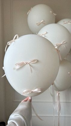 a bunch of white balloons are being held by someone's hand with ribbons on them