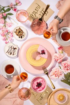 a table topped with plates and cups filled with desserts next to pink flowered napkins