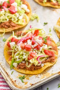 three tacos with meat, lettuce and tomatoes on a baking sheet ready to go into the oven