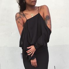 a woman in a black dress with tattoos on her arm