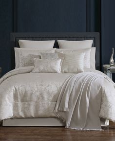 a bed with white comforter and pillows in a dark blue room next to a night stand