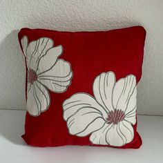 a red pillow with white flowers on it sitting on a table next to a wall