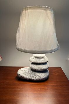 a lamp sitting on top of a wooden table next to a pile of rocks under a shade