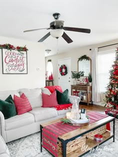 a living room decorated for christmas with red and green decorations on the walls, white couches and a coffee table