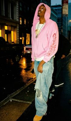 a man in a pink hoodie is standing on the sidewalk