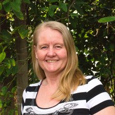 a woman in striped shirt standing next to a tree and smiling at the camera with green leaves behind her