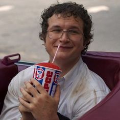 a man with curly hair and glasses is holding a drink in his hand while smiling