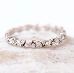 a white gold wedding band with diamonds on the sides and leaves in the middle, sitting on a rock