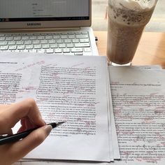 someone is writing on paper next to a laptop and a glass of coffee with a beverage in it