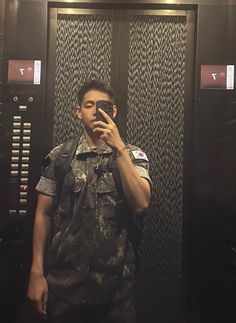 a man taking a selfie in front of a wall mounted elevator with his cell phone