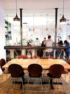 a group of people standing at a bar in a restaurant with wooden tables and chairs