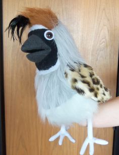 a hand holding a stuffed bird on top of a wooden door handle with fake feathers