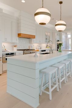 a large kitchen with white cabinets and counter tops, along with bar stools that match the hardwood flooring