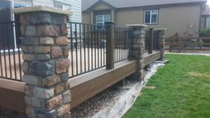 a wooden deck with black iron railings and stone pillars in front of a house