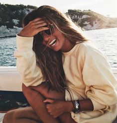 a woman sitting on the back of a boat with her hands in her hair and smiling