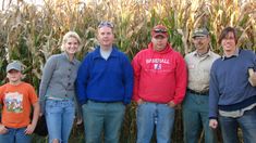 a group of people standing next to each other in front of a corn field