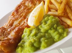 fish and chips are served on a white plate with green sauce, as well as lemon wedges