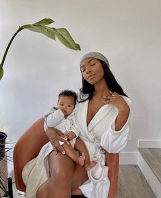 a woman holding a baby in her lap while sitting on a chair next to a potted plant