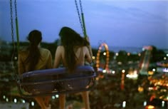 two women sitting on swings overlooking a city at night