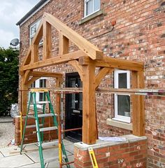 a house being built in front of a brick building with a wooden structure on the side