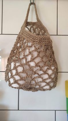 a crocheted bag hanging from a hook on a tiled wall in a bathroom