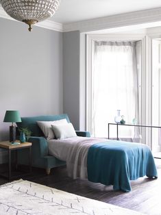 a bed sitting next to a blue couch in a bedroom under a chandelier