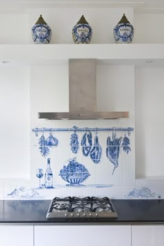 a kitchen with blue and white tiles on the backsplash, stove top and cabinets