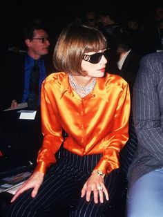 a woman in an orange shirt and striped pants sitting next to a man wearing a suit