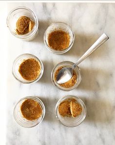 four small glass jars filled with food on top of a marble counter next to a spoon