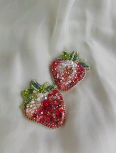 two strawberry shaped brooches are laying on a white cloth covered with sequins