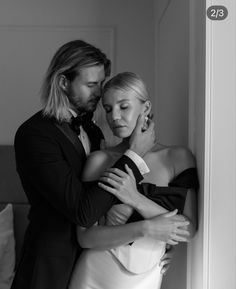 a man standing next to a woman in a dress and tuxedo hugging her