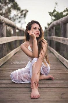 a beautiful young woman sitting on top of a wooden bridge