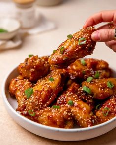 a person dipping sauce on top of chicken wings in a white bowl with chopsticks