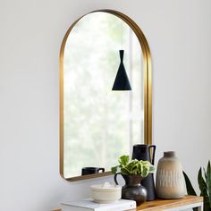 a mirror and some vases on a table with a potted plant in front of it