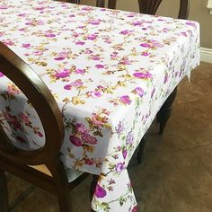 a dining room table covered with a white and pink floral tablecloth next to two wooden chairs