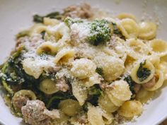 a white bowl filled with pasta and broccoli covered in parmesan cheese