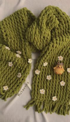 a green knitted scarf with white flowers and a yellow bird on the front, sitting on a white sheet