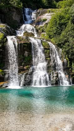 a large waterfall in the middle of a forest filled with green trees and blue water