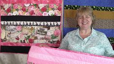 an older woman holding up a quilt made with pink and black fabric, in front of a wall hanging