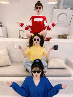 three women sitting on top of each other in the middle of a room with white furniture