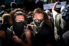 two people wearing face masks in the middle of a crowd with cameramen behind them