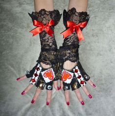 two hands wearing black lace gloves with red bows and hearts on them, both holding onto each other's fingers