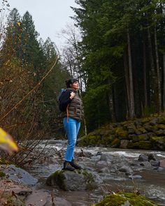 a woman with a backpack is standing on rocks in the middle of a river and looking at something