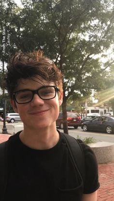 a young man wearing glasses standing in front of a tree