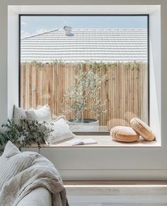 an open window in a living room with pillows and blankets on the windowsill, next to a potted plant