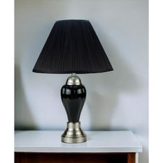 a black lamp sitting on top of a white table next to a wooden cabinet with drawers