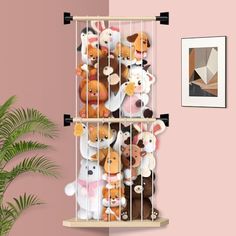 stuffed animals are placed in a cage on the wall next to a potted plant