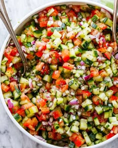 cucumber and tomato salad in a white bowl with two spoons on the side