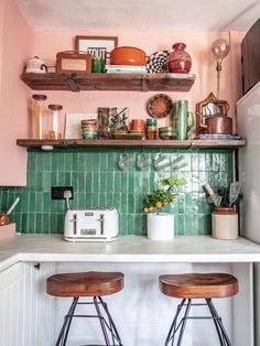 two wooden stools sit in front of a green tiled kitchen counter with pots and pans on it