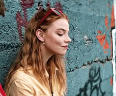 a woman with red hair and sunglasses leaning against a wall